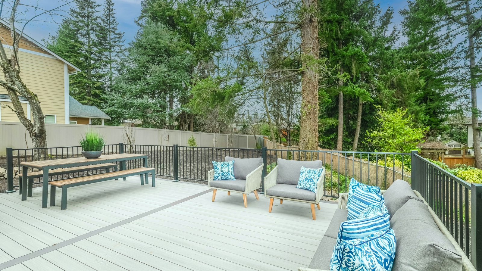 Light gray composite backyard deck with a metal railing, outdoor chairs and a dining bench